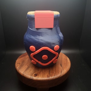 May include: A blue ceramic jar with a red lid and a red geometric design. The jar is sitting on a wooden base.