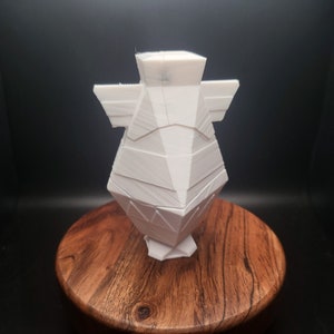 May include: White ceramic vase with a geometric design. The vase has a square base and a wide, open top.
