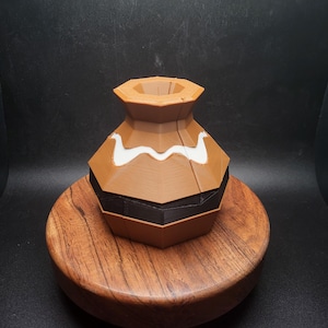 Puede incluir: Un jarrón geométrico marrón y negro con un diseño de ondas blancas. El jarrón está hecho de materiales en capas y descansa sobre un soporte de madera. El jarrón tiene una base ancha y un cuello estrecho.