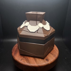 May include: A brown, intricately designed, puzzle box with white accents. The box is made of multiple pieces that fit together.