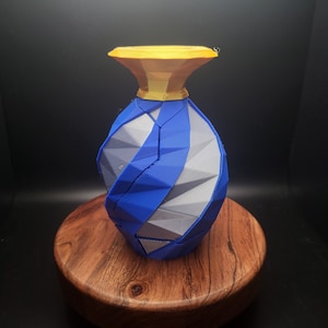 Könnte beinhalten: Eine blaue und weiße geometrische Vase mit goldener Oberseite. Die Vase ist aus 3D-gedrucktem Kunststoff gefertigt und hat ein einzigartiges, modernes Design.