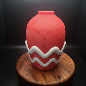 May include: A red ceramic vase with a white wavy design around the bottom. The vase is made of multiple pieces that fit together.