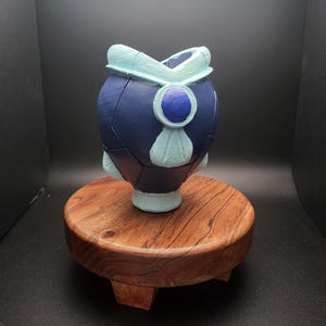 May include: A blue and white ceramic vase with a geometric design. The vase is sitting on a wooden pedestal.