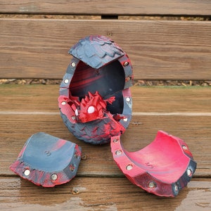 May include: A red and black dragon egg toy with a small red dragon inside. The egg is broken into several pieces, revealing the dragon inside.