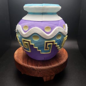 May include: A purple and blue ceramic pot with a white and yellow geometric design. The pot is sitting on a wooden base.