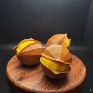 May include: Three brown, geometrically shaped, chocolate candies with yellow centers. The candies are sitting on a wooden surface.