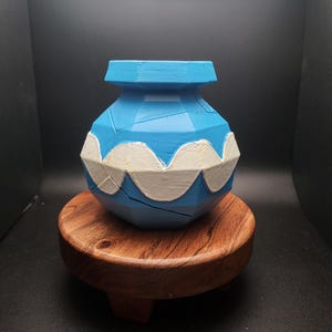 May include: A blue and white ceramic pot with a geometric design. The pot is sitting on a wooden stand.