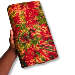 May include: A folded piece of fabric featuring a vibrant tie-dye pattern with bold splashes of red, deep green, and warm orange tones. The textile displays an abstract, organic design with blended colours throughout the entire surface area.