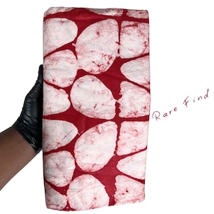 May include: A folded fabric featuring a red backdrop with large white, irregular shapes. The fabric is held by a gloved hand. The words "Rare Find" are written in cursive.