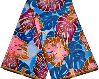 May include: A folded length of fabric featuring a vibrant tropical pattern of large monstera leaves in shades of pink, magenta, and deep blue against a light blue background. The fabric edges have a brown border with the text GOLD JAVA 8234808.