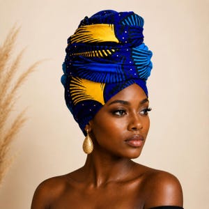 Puede incluir: Un pañuelo para la cabeza con un patrón vibrante de motivos en forma de abanico en azul profundo y amarillo brillante con pequeños puntos blancos. La tela está intrincadamente doblada y envuelta alrededor de la cabeza, creando volumen.