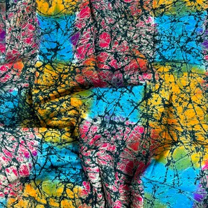 Puede incluir: Una tela colorida con un patr&oacute;n batik en tonos de azul, amarillo, rosa y negro. La tela tiene una textura arrugada y est&aacute; doblada en el centro.