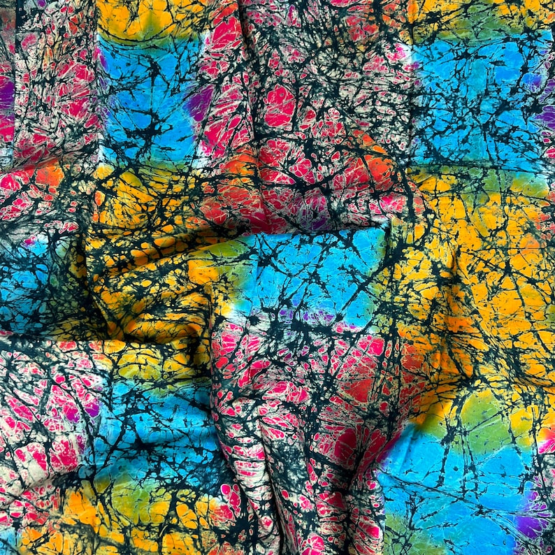 Puede incluir: Una tela colorida con un patr&oacute;n batik en tonos de azul, amarillo, rosa y negro. La tela tiene una textura arrugada y est&aacute; doblada en el centro.
