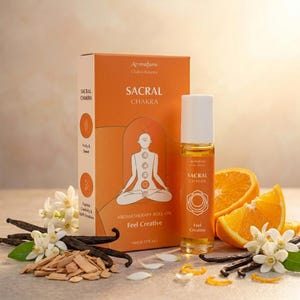 May include: An orange box and roll-on bottle with the text "SACRAL CHAKRA" and "Feel Creative". The box features a white illustration of a person meditating. Sliced oranges, vanilla beans, and flowers are arranged around the products.