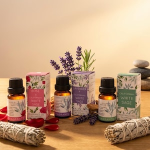 May include: An assortment of essential oil bottles with black caps and decorative boxes. The boxes are labeled with the scents: Rose, Lavender, and Californian White Sage. Dried sage bundles and flower sprigs are also present.