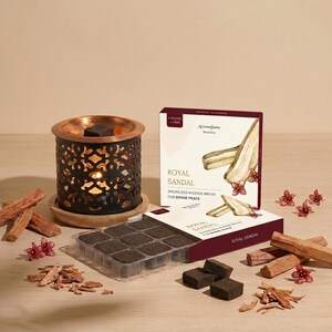 May include: A black metal incense burner with a copper top and intricate cut-out design. The image also shows a box of "Royal Sandal" smokeless incense bricks, incense bricks, and wood chips. The text on the box reads "Royal Sandal" and "Smokeless Incense Bricks for Divine Peace."