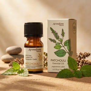 May include: A small amber glass bottle of Aromafume Naturals Patchouli essential oil with a black cap, next to its matching white cardboard box featuring a botanical illustration of the plant and the text 0.33 fl oz (10ml) on the label.