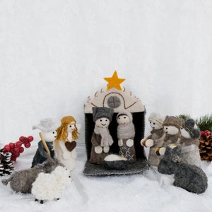 May include: A handcrafted Christmas nativity scene featuring felt figures. The scene includes Mary, Joseph, baby Jesus in a manger, angels, shepherds, and animals. The figures are dressed in gray, brown, and white, with a star atop the stable.