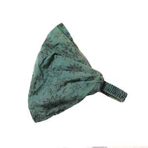 May include: A teal fabric headband featuring a repeating black print of suns, stars, and crescent moons. The accessory has a gathered, wide top section and a narrow, elasticated band at the back to provide a secure fit for the wearer.