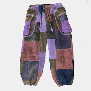 May include: Patchwork corduroy pants featuring an elastic waistband with a drawstring. The trousers are constructed from rectangular panels in shades of olive green, purple, maroon, and navy blue, including two side cargo pockets with zippers.