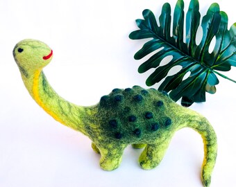 May include: A green felt dinosaur toy with a long neck and a yellow stripe down the neck. The dinosaur has dark green spots on its back and tail.
