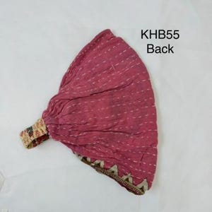 May include: A magenta fabric headwrap featuring white horizontal running stitch details and a patterned elastic band. The text KHB55 Back is printed in black near the top right corner. The fabric has a gathered texture and a decorative border.
