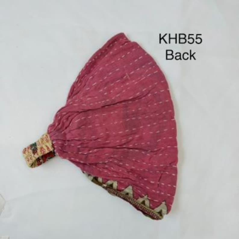 May include: A magenta fabric headwrap featuring white horizontal running stitch details and a patterned elastic band. The text KHB55 Back is printed in black near the top right corner. The fabric has a gathered texture and a decorative border.