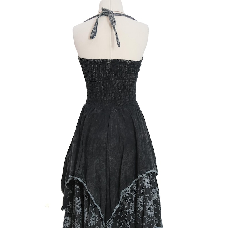 May include: A black halter dress with a smocked bodice and a tie-neck closure. The skirt features an uneven hemline with a distressed wash finish. The lower portion of the skirt displays a repeating pattern of white suns, moons, and stars on black fabric.
