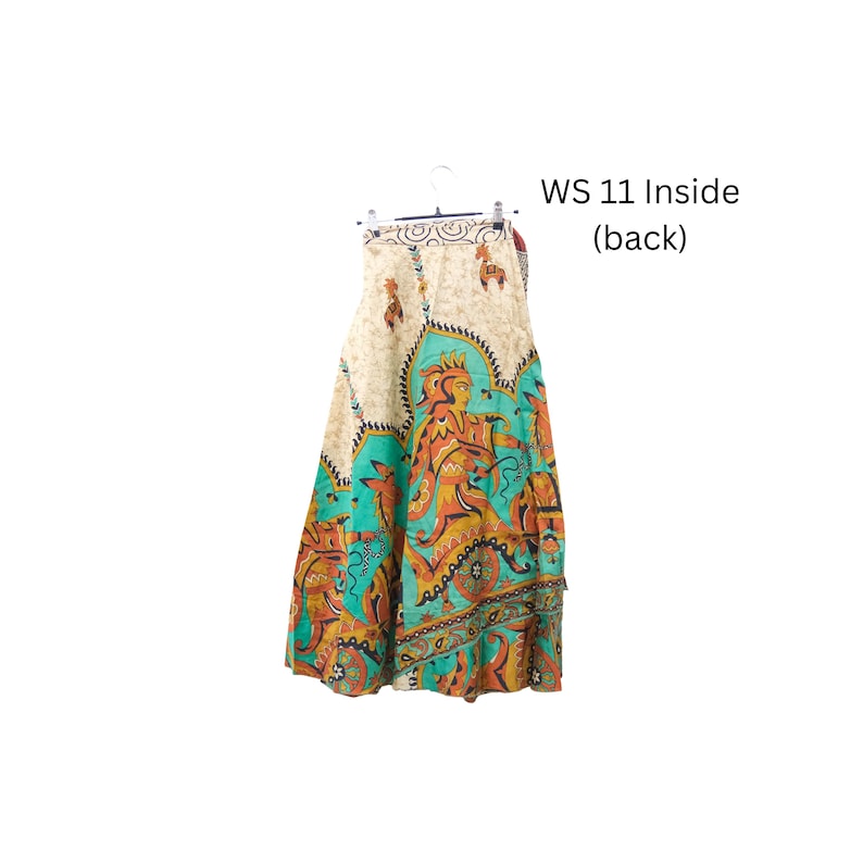 Op de afbeelding: Een lange rok met een cr&egrave;mekleurige tailleband met kleine bruine diermotieven en een levendig onderste gedeelte met turquoise, oranje en gele patronen die gestileerde figuren en dieren afbeelden. De tekst WS 11 Inside (back) is zichtbaar.
