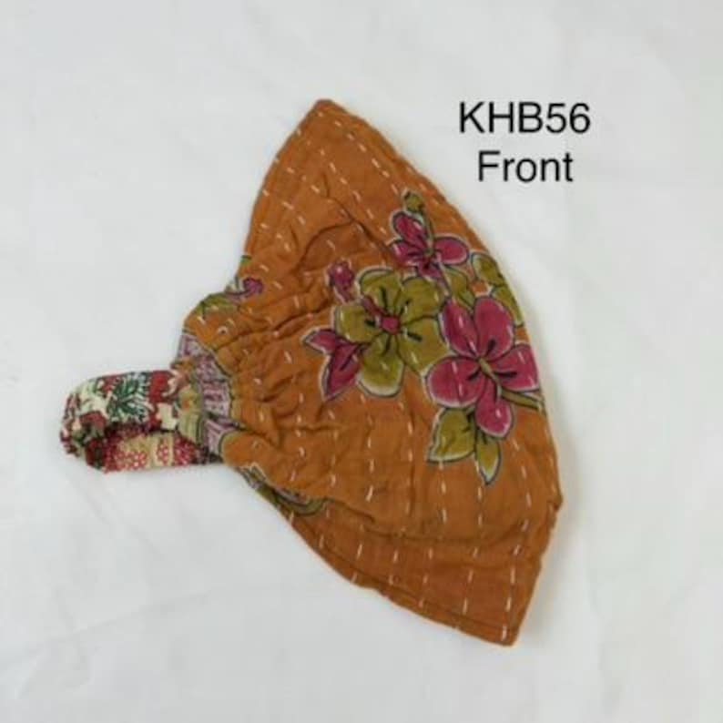 May include: A mustard-colored fabric headwrap featuring a floral pattern with pink and green petals, accented by white running stitch details. The item includes an elasticized band with a multi-colored print and is labeled with the text KHB56 Front.
