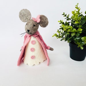 May include: A handmade felt mouse figure with large grey ears and a pink bow. The mouse wears a white dress with pink buttons and a pink coat. A charming decorative item.