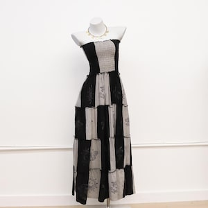 May include: A strapless maxi dress featuring a smocked bodice and a patchwork design of alternating black and light gray panels. The gray panels are decorated with black celestial and butterfly prints. The dress is displayed on a white mannequin.