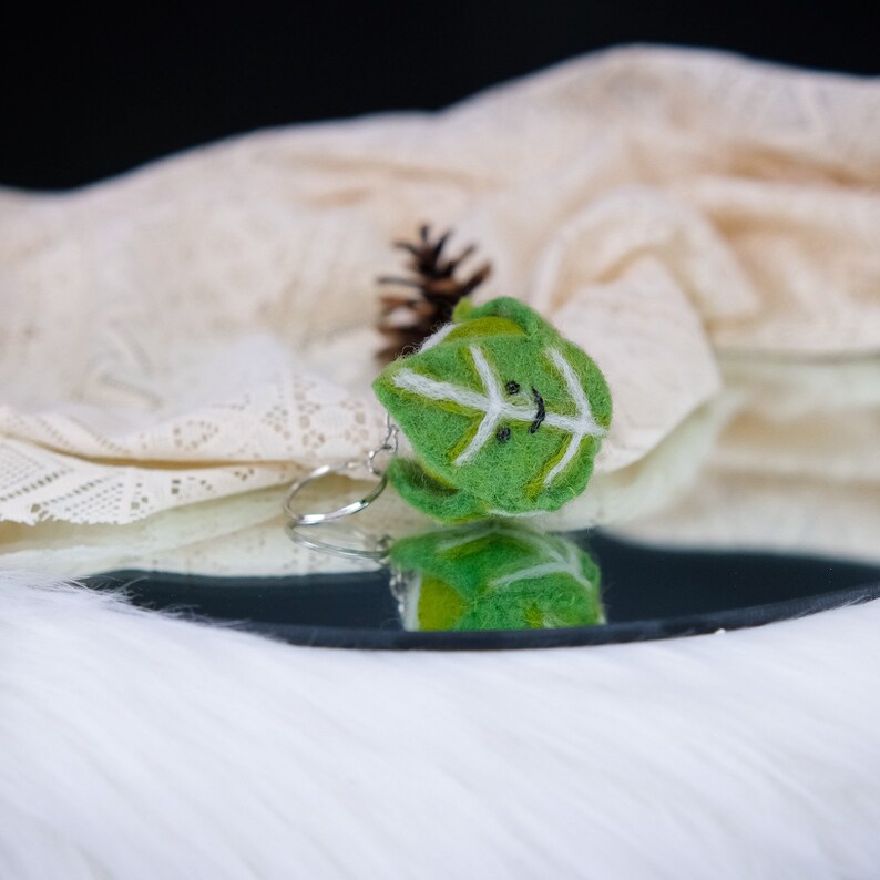 May include: A green felt leaf keychain with a white smiling face and a silver key ring.