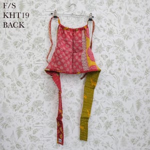 May include: A halter-style top featuring a pink fabric panel with a spiral pattern, accented by a yellow side border and long, dangling straps in red and olive green. The garment is suspended from a metal hanger and displays the text F/S KHT19 BACK.