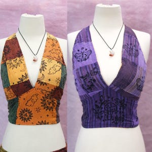 Könnte beinhalten: Zwei Neckholder-Tops auf Schaufensterpuppen. Das linke Top hat ein Patchwork-Design in Orange, Braun und Grün mit Sonnen-, Mond- und Wolkenmotiven. Das rechte Top ist violett, gestreift und mit schwarzen Motiven von Motten, Schmetterlingen und Pilzen bedruckt.