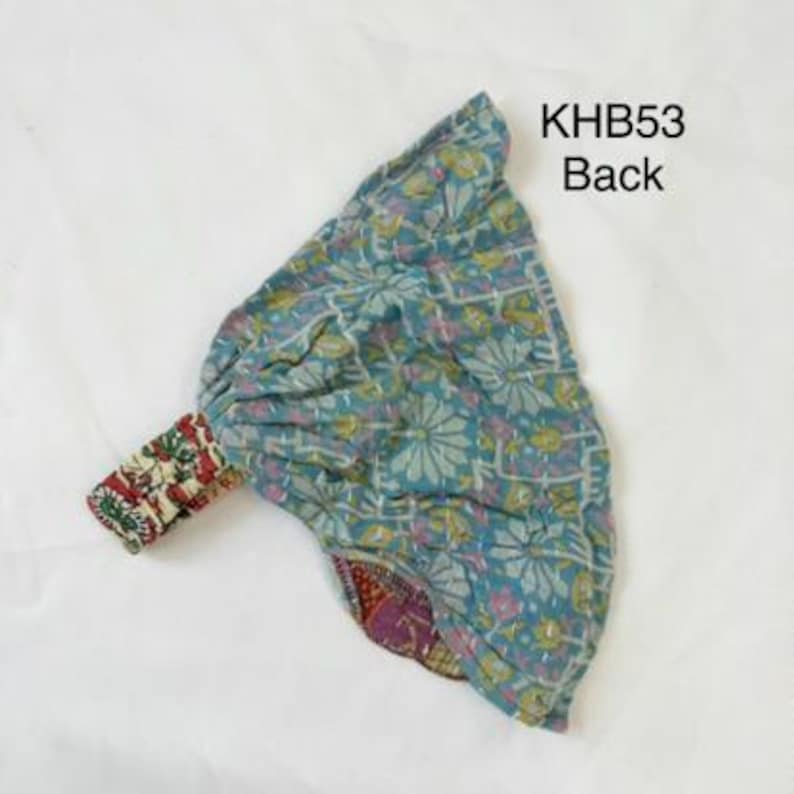 May include: A teal fabric headband with a floral pattern and white stitching, featuring a gathered design and a contrasting red and white patterned elastic strap. The text KHB53 Back is printed in black in the upper right corner of the image.