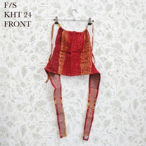 May include: A red and gold patterned halter top featuring a gathered neckline and long fabric ties. The garment displays a textured, stitched appearance with vertical stripes and includes the text F/S KHT 24 FRONT printed in the upper left corner.