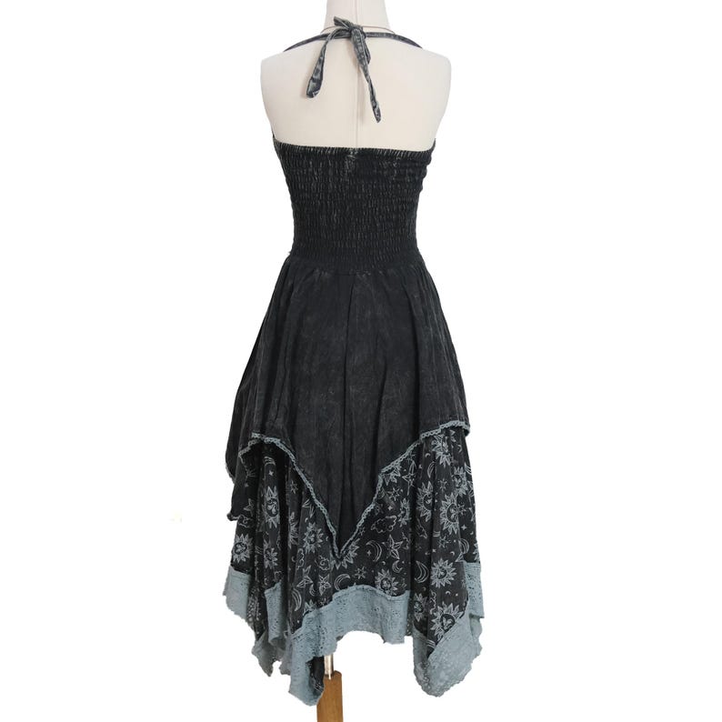 May include: A black halter dress with a smocked bodice and a tie-neck closure. The skirt features an asymmetrical handkerchief hemline with a layered design, showcasing a grey celestial print of suns, moons, and stars on the lower panel.