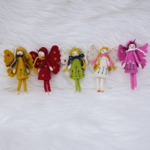 Può includere: Cinque ornamenti di fata in feltro con ali, ognuno in un colore diverso: giallo, rosso, verde, bianco e rosa. Ogni fata ha un diverso motivo floreale sul suo vestito e sulle sue ali.