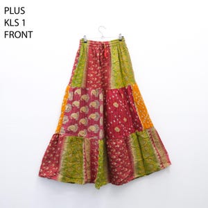 May include: A patchwork skirt in shades of red, green, yellow, and orange, hanging on a hanger. The skirt features various patterned fabric panels, including paisley and dotted designs. The text "PLUS KLS 1 FRONT" is visible.