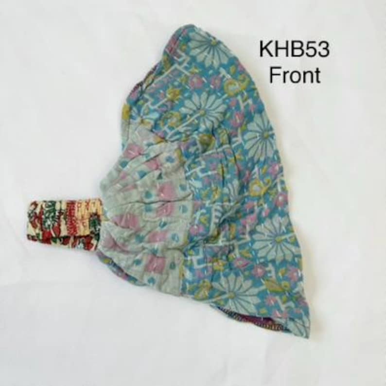 May include: A fabric headband labeled KHB53 Front, featuring a teal base with a white and pink floral pattern. The band includes a gathered section and a contrasting strap with a red, green, and white intricate print, showcasing visible stitching.