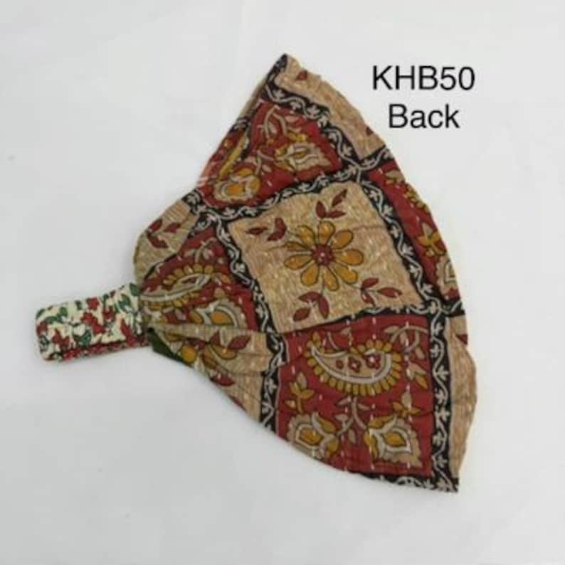 May include: A fabric headband featuring a patchwork design with floral and paisley patterns in shades of red, tan, and yellow. The accessory includes a gathered elastic band section and is labeled with the text KHB50 Back in the upper right corner.