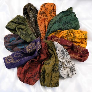 May include: A collection of ten fabric headbands arranged in a circular pattern. Each headband features a repeating print of suns, moons, stars, and clouds in various colours including orange, green, yellow, purple, red, brown, and white.