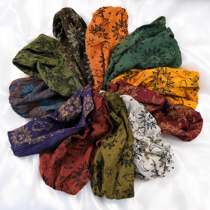 May include: A collection of ten fabric headbands arranged in a circular pattern. Each headband features a repeating print of suns, moons, stars, and clouds in various colours including orange, green, yellow, purple, red, brown, and white.