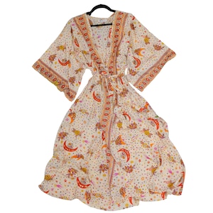 May include: A cream-colored wrap dress featuring a repeating pattern of orange crescent moons, stars, and floral motifs. The garment has wide, three-quarter length sleeves, a V-neckline, and a matching fabric tie belt at the waist.