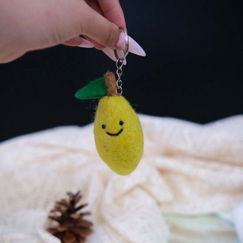 May include: A yellow felt lemon keychain with a green felt leaf and a smiling face. The keychain is attached to a silver key ring.