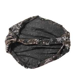May include: A black fabric headband featuring a white celestial print of suns, moons, and stars. The accessory has a gathered design with an elasticated band at the back to provide a secure fit, showcasing a repeating pattern across the entire surface.