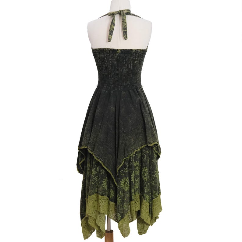 May include: A dark charcoal gray and olive green halter dress featuring a smocked bodice and a tie-neck closure. The skirt has an asymmetrical handkerchief hemline with a layered design, showcasing a sun, moon, and star print on the lower panel.