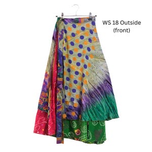 Op de afbeelding: Een wikkelrok met een veelkleurig patroon met paarse stippen op een lichte achtergrond, overgaand in groene, roze en paarse bloemen- en geometrische secties. De tekst WS 18 Outside (front) is zichtbaar aan de rechterbovenkant van de afbeelding.