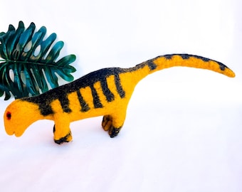 May include: A yellow and black felt dinosaur toy with a long neck and tail. The dinosaur is lying on its belly with its head turned to the side.